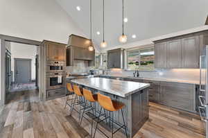 Kitchen with light hardwood / wood-style flooring, tasteful backsplash, a center island, and high vaulted ceiling