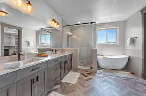 Bathroom featuring a textured ceiling, separate shower and tub, dual bowl vanity, tile walls, and parquet floors