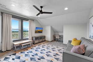 Carpeted living room with ceiling fan, vaulted ceiling, and a textured ceiling