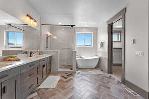 Bathroom featuring a textured ceiling, parquet flooring, vanity, and separate shower and tub