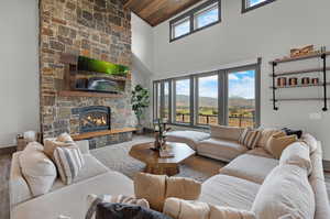 Living room with high vaulted ceiling, wood-type flooring, a stone fireplace, and wooden ceiling