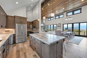 Kitchen featuring stainless steel fridge, high vaulted ceiling, a center island, light hardwood / wood-style floors, and backsplash