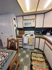 Kitchen with tile patterned floors, white appliances, and white cabinetry