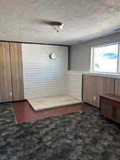 Interior space with a textured ceiling, wooden walls, and brick wall