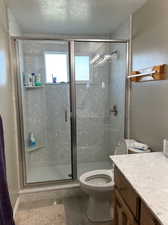 Bathroom with a textured ceiling, walk in shower, toilet, and vanity