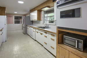 Kitchen with white cabinets, sink, white appliances, and light tile patterned floors