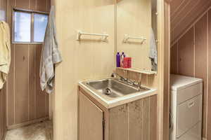 Washroom with washer / clothes dryer, light tile patterned flooring, wood walls, and sink