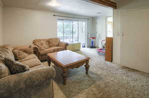 Carpeted living room with ornamental molding and beam ceiling