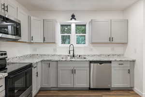 Kitchen with dark hardwood / wood-style floors, gray cabinetry, sink, and stainless steel appliances