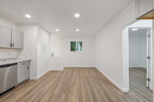 Kitchen featuring hardwood / wood-style floors, gray cabinets, stainless steel dishwasher, and light stone countertops