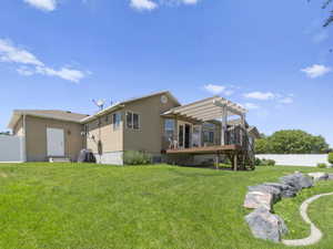 Rear view of property with a wooden deck, a pergola, and a lawn.