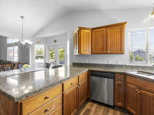 Kitchen with lofted ceiling, dark hardwood / wood-style flooring, a notable chandelier, dishwasher, and kitchen peninsula.