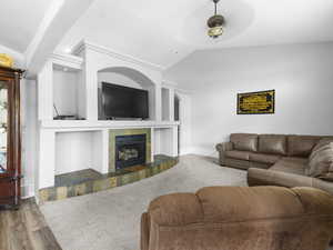 Living room featuring ceiling fan, lofted ceiling, carpet flooring, a slate tiled fireplace, and built in features.