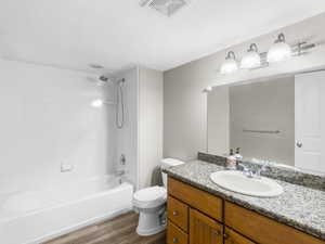 Full basement bathroom featuring a textured ceiling, bathing tub / shower combination, toilet, LVP flooring, and vanity. Freshly glazed tub and shower surrond.