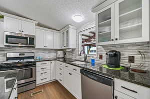 Kitchen with dark stone countertops, dark hardwood / wood-style flooring, decorative backsplash, appliances with stainless steel finishes, and sink