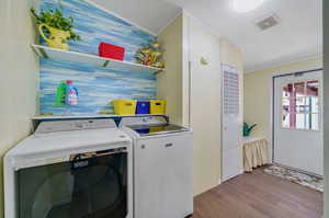 Clothes washing area with a textured ceiling, washer and dryer, and wood-type flooring