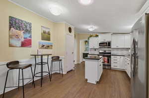 Kitchen with decorative backsplash, white cabinetry, appliances with stainless steel finishes, a center island, and dark hardwood / wood-style flooring