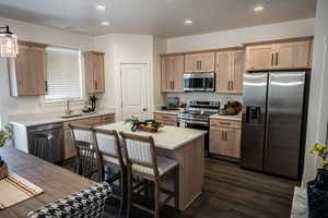 Kitchen featuring dark hardwood / wood-style floors, appliances with stainless steel finishes, a kitchen bar, sink, and a center island