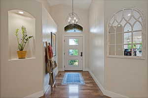 Foyer entrance with dark wood-type flooring, a chandelier, and vaulted ceiling