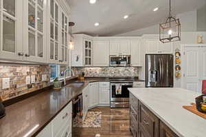 Kitchen with appliances with stainless steel finishes, sink, vaulted ceiling, and decorative light fixtures