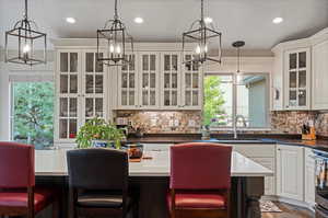 Kitchen featuring a kitchen bar, white cabinetry, pendant lighting, backsplash, and sink