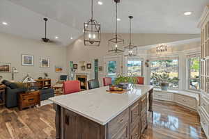 Kitchen featuring hanging light fixtures, wood-type flooring, vaulted ceiling, a kitchen island, and light stone counters