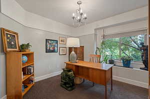 Bedroom used as a home office featuring a notable chandelier and dark carpet