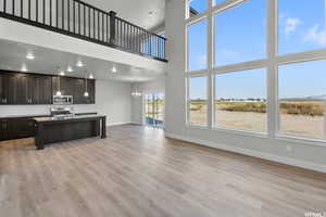 Kitchen featuring light wood-type flooring, appliances with stainless steel finishes, an island with sink, decorative backsplash, and a towering ceiling