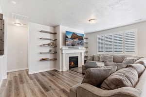 Living room with a tiled fireplace, a textured ceiling, and light wood-type flooring