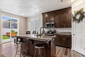 Kitchen featuring decorative backsplash, a center island with sink, light hardwood / wood-style floors, stainless steel appliances, and a breakfast bar