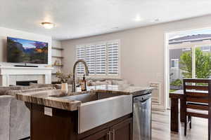 Kitchen featuring a textured ceiling, dishwasher, dark brown cabinets, a tile fireplace, and light hardwood / wood-style flooring