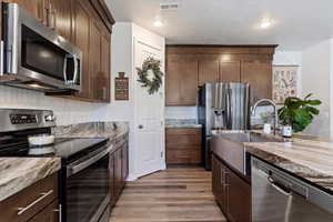 Kitchen with a textured ceiling, appliances with stainless steel finishes, light hardwood / wood-style floors, light stone countertops, and sink