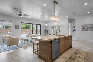 Kitchen featuring sink, decorative light fixtures, stainless steel dishwasher, and an island with sink