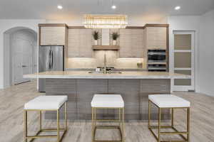 Kitchen with stainless steel appliances, an inviting chandelier, backsplash, a kitchen island with sink, and light brown cabinetry