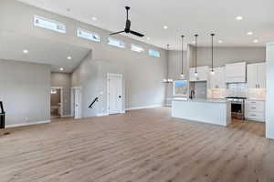 Kitchen featuring stainless steel range with gas cooktop, light wood-type flooring, and a high ceiling