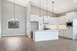 Kitchen with stainless steel microwave, decorative backsplash, white cabinetry, high vaulted ceiling, and light hardwood / wood-style floors