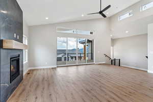 Unfurnished living room with high vaulted ceiling, a fireplace, ceiling fan, and light hardwood / wood-style floors