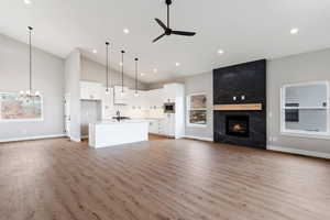 Unfurnished living room featuring light hardwood / wood-style flooring, a fireplace, high vaulted ceiling, and ceiling fan with notable chandelier