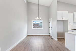 Unfurnished dining area with a notable chandelier, light hardwood / wood-style flooring, and high vaulted ceiling