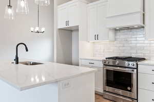 Kitchen featuring white cabinets, light stone countertops, light wood-type flooring, backsplash, and stainless steel gas range