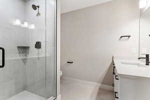 Bathroom with a shower with door, vanity, tile patterned floors, and toilet