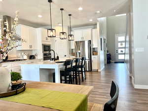 Kitchen with pendant lighting, hardwood / wood-style floors, appliances with stainless steel finishes, an island with sink, and white cabinets