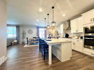 Kitchen featuring wall chimney range hood, an island with sink, dark hardwood / wood-style flooring, and a wealth of natural light