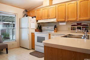 Kitchen featuring sink, vaulted ceiling, light tile patterned flooring, and white appliances