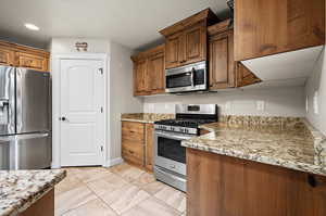 Kitchen with light tile patterned floors, stainless steel appliances, and light marble countertops