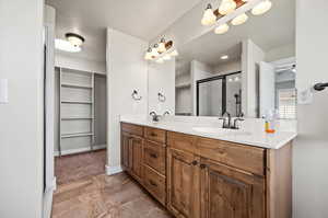 Primary Bathroom featuring ceiling fan, tile patterned floors, double sink vanity,  enclosed shower, large walk-in closet with sky light