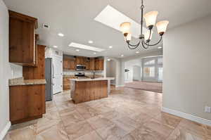 Kitchen featuring a center island with sink, stainless steel appliances, a chandelier, light colored tile, decorative light fixtures, skylights, view of Great Room and patio entrance