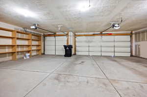 3 car Garage featuring built in shelves, ceiling pull down stairs for more storage access, and a garage door opener