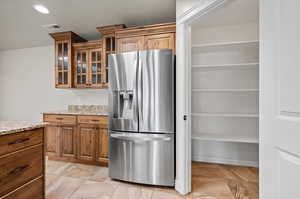 Kitchen with light tile patterned flooring, stainless steel refrigerator with ice dispenser, light marble counters, cupboards, and large pantry