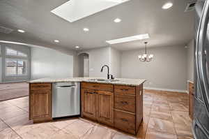 Kitchen featuring appliances with stainless steel finishes, light marble countertops, a skylight, light tile patterned floors, sink, and dining area